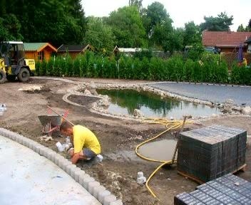 Ein Mitarbeiter der Hirsch Gruppe verlegt Randsteine an einer Baustelle für einen Naturteich; im Hintergrund ist ein gelber Radlader zu sehen.