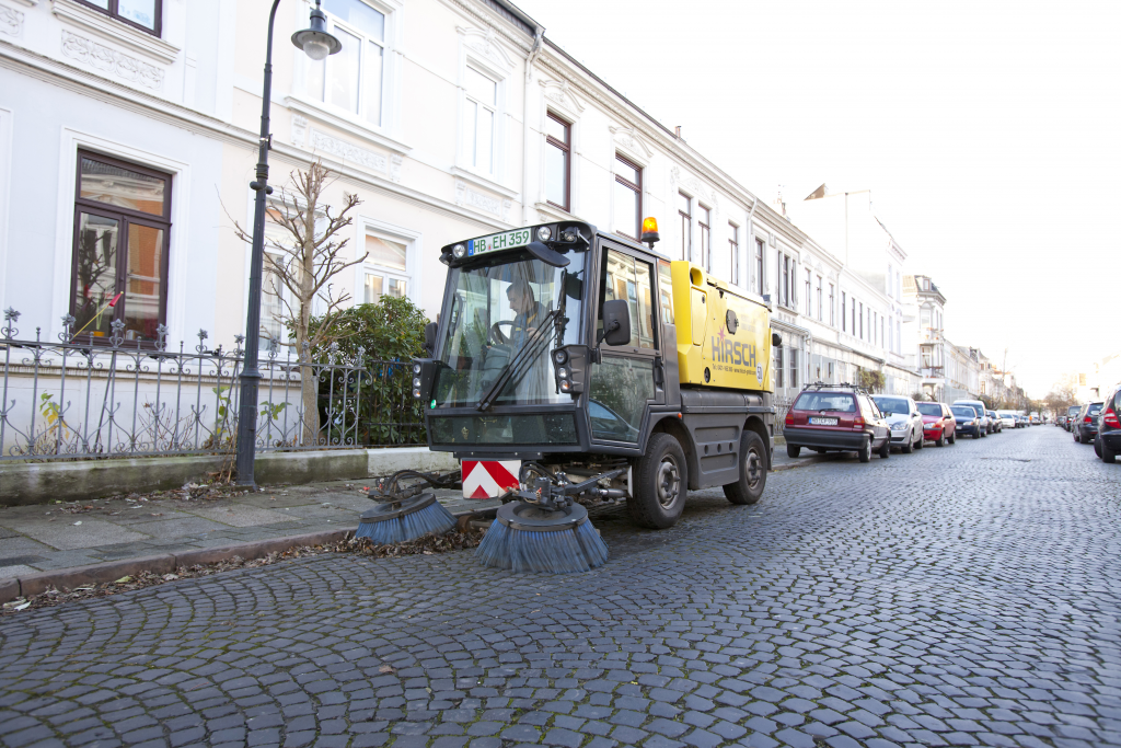 Frontansicht eines gelben Reinigungsfahrzeugs der Hirsch Gruppe (Kennzeichen HB-EH 359) in einer historischen Wohnstraße mit Altbauten.